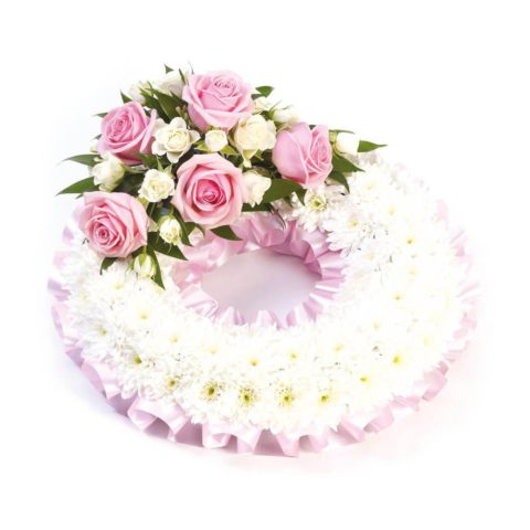 A classic circular wreath covered with a mass of white double spray chrysanthemums and finished with a pink and white spray of roses and spray roses and finished with a pink ribbon trim.